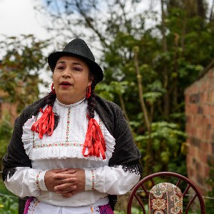 A rural woman dressed traditionally with a black hat and red ribbons on her hair. 
