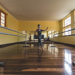 Woman dancing in the middle of a specialized wooden-floor room. 