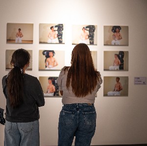 Two women analyzing a group of paintings on the wall. 
