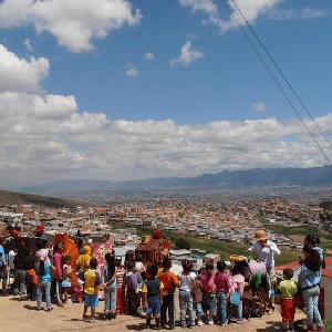 Many kids and adults standing on top of a hill with the city on the back.