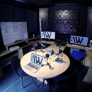 A radio cabin with a circular desk in the middle. Three computer screens display CKWEB’s logo on a colored background.